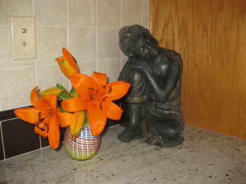 Statue of a sitting Buddha with a vase of orange lilies.